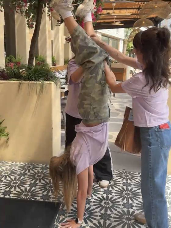 Two of the team spotting a third doing a handstand on the sidewalk outside a restaurant