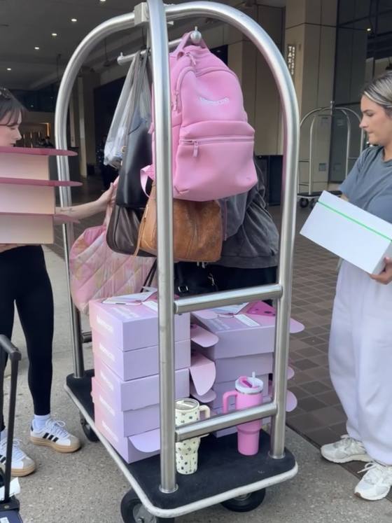 A hotel luggage cart stacked with Momeaze boxes, a pink Momeaze backpack and a display shelf, being wheeled in for an event