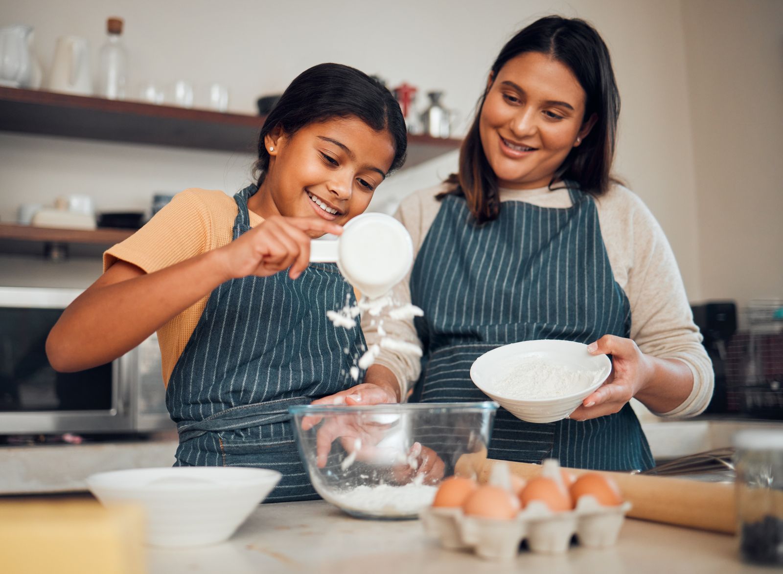 A mother and daughter baking together in aprons