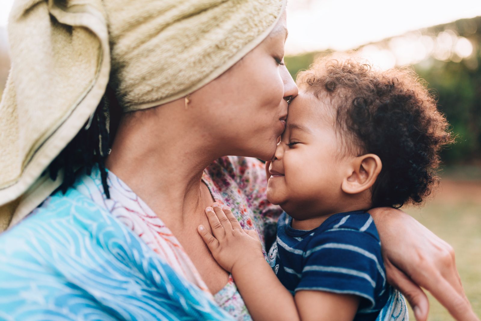 A mother kissing her small child on the forehead outdoors