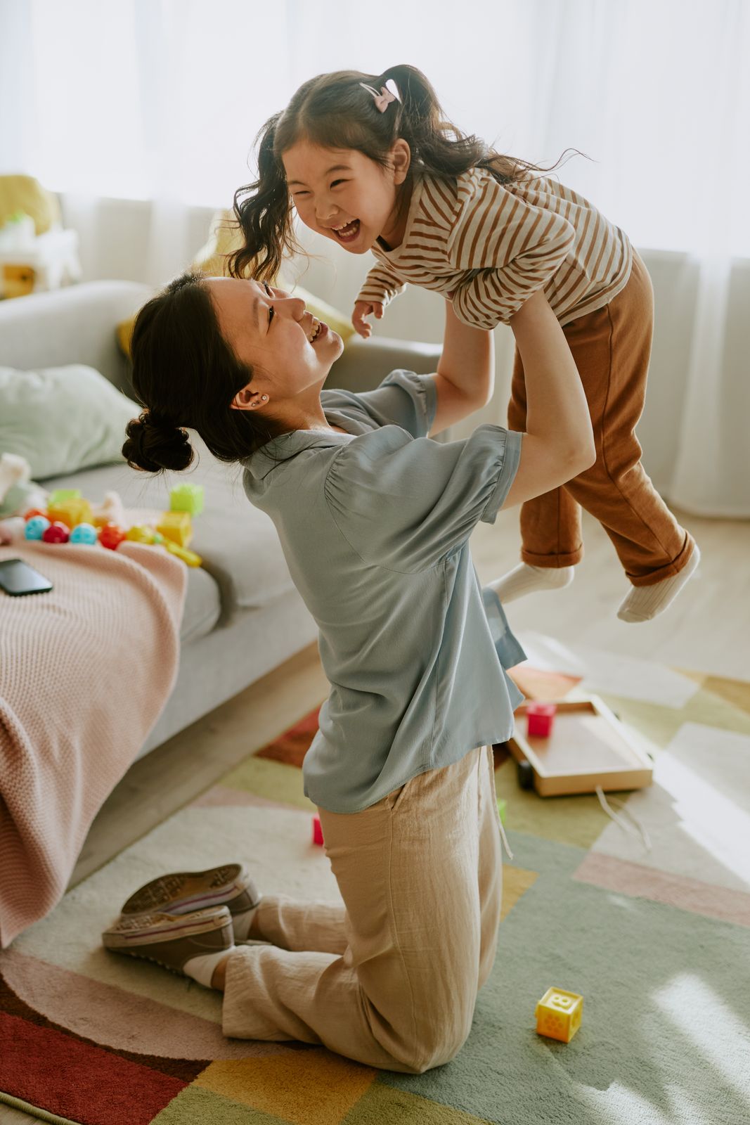 A mother lifting her laughing toddler above her head in a bright living room